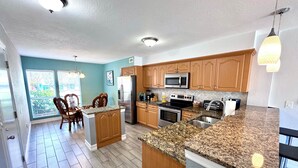 A kitchen with granite countertops, wooden cabinets, stainless steel appliances, and a dining area with wicker chairs.