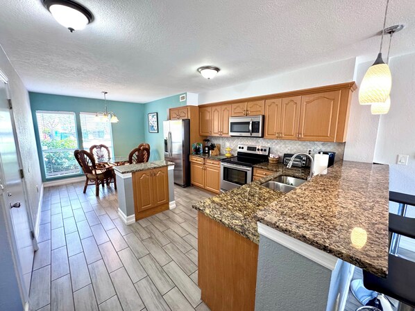 A kitchen with granite countertops, wooden cabinets, stainless steel appliances, and a dining area with wicker chairs.