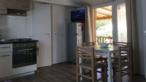 Pieni, käytännöllinen keittiö, jossa on liesi, uuni ja jääkaapin yläpuolelle asennettu televisio.