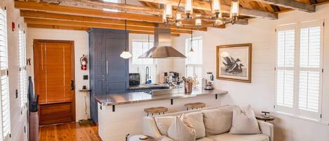 Un salon chaleureux avec un plafond en bois, un canapé, une table basse et, au fond, un coin cuisine.