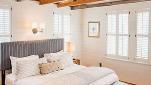 A bedroom with a large bed, wooden beams, and a window with shutters. - King Bed Suite | Claw-Foot Tub, Chef Kitchen & Parking | Downtown Charleston (Charleston)