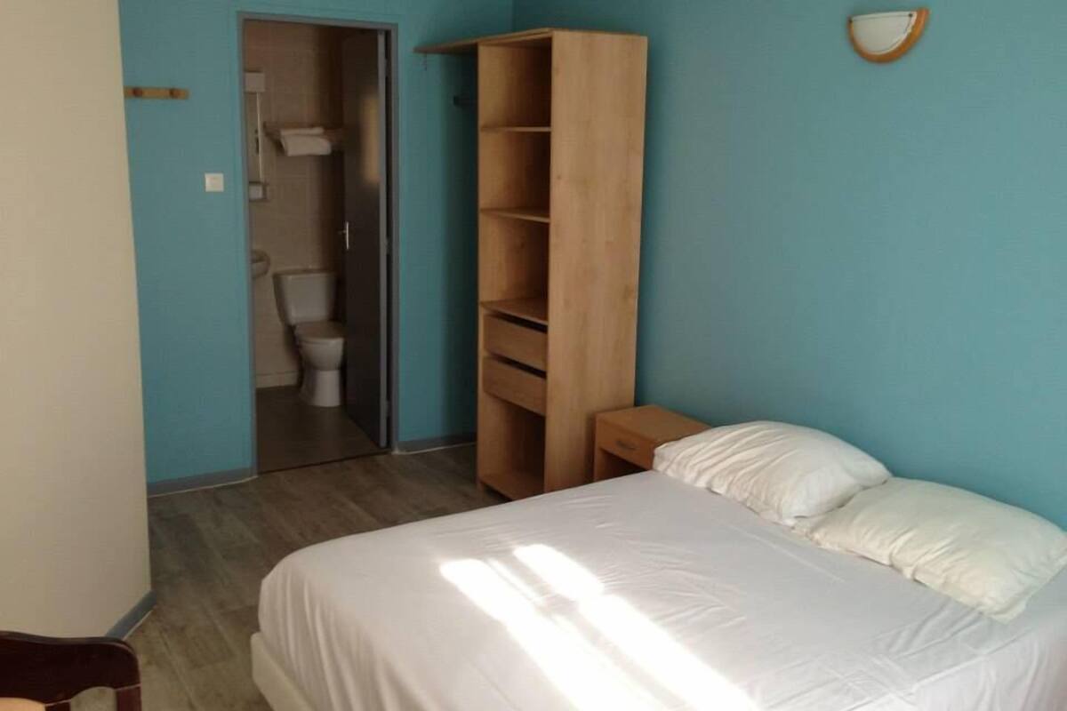 Un dormitorio con cama, un armario de madera y un baño que se ve a través de una puerta abierta.