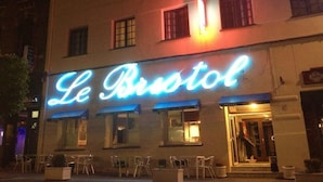 Un hotel llamado "Le Bristol" con un letrero de neón, zona de estar al aire libre y una entrada visible.