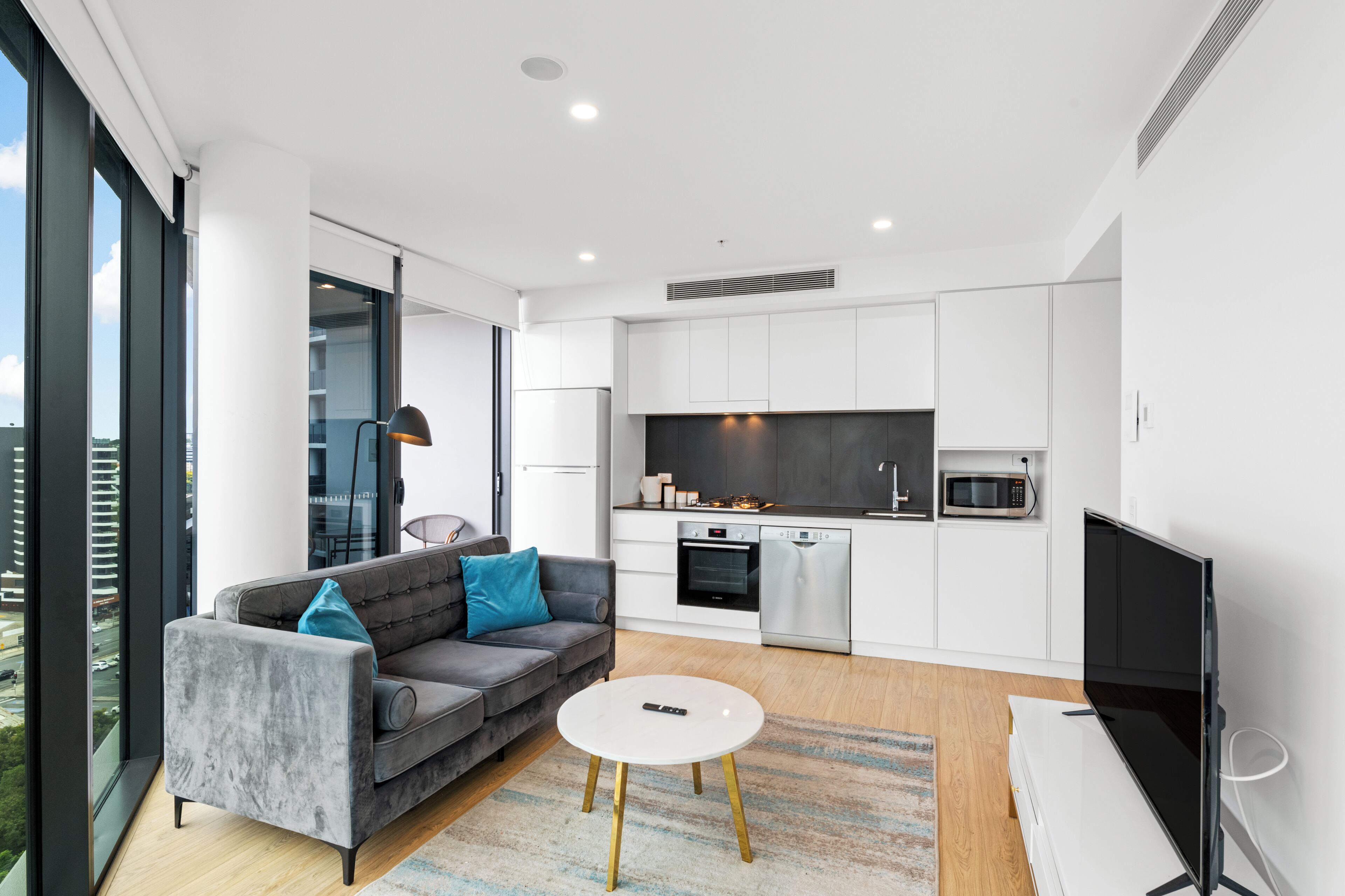 A modern living room with a grey sofa, a white coffee table, and a flat-screen TV.