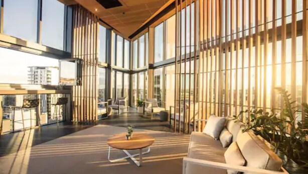 A modern interior with a sofa, a coffee table, and a view of the city through large windows. - Brisbane One Apartments by CLLIX (South Brisbane)