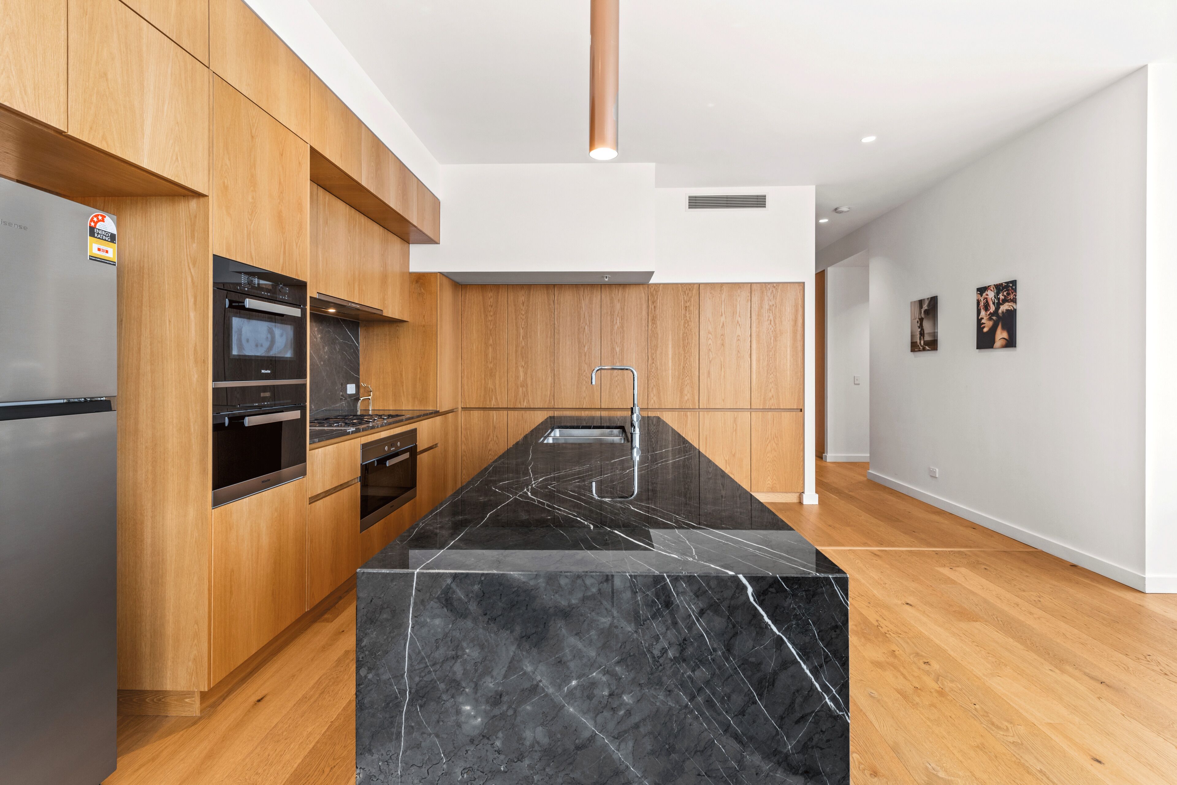 Een moderne keuken met houten kastjes, een zwart marmeren aanrechtblad, roestvrijstalen apparatuur en een houten vloer.