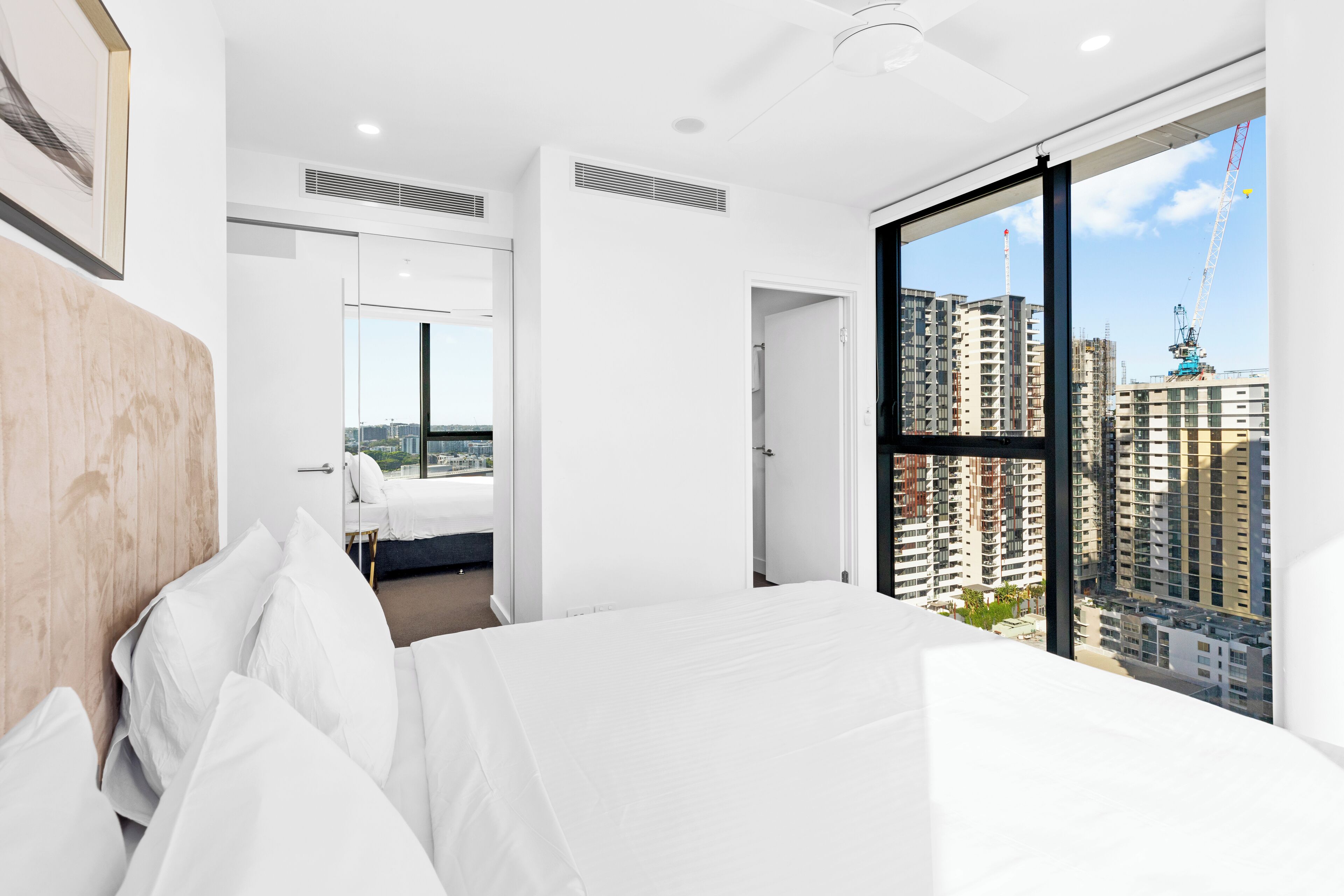 Ein modernes Hotelzimmer mit einem großen Bett, Blick auf die Stadtlandschaft und einer Tür zum Badezimmer.