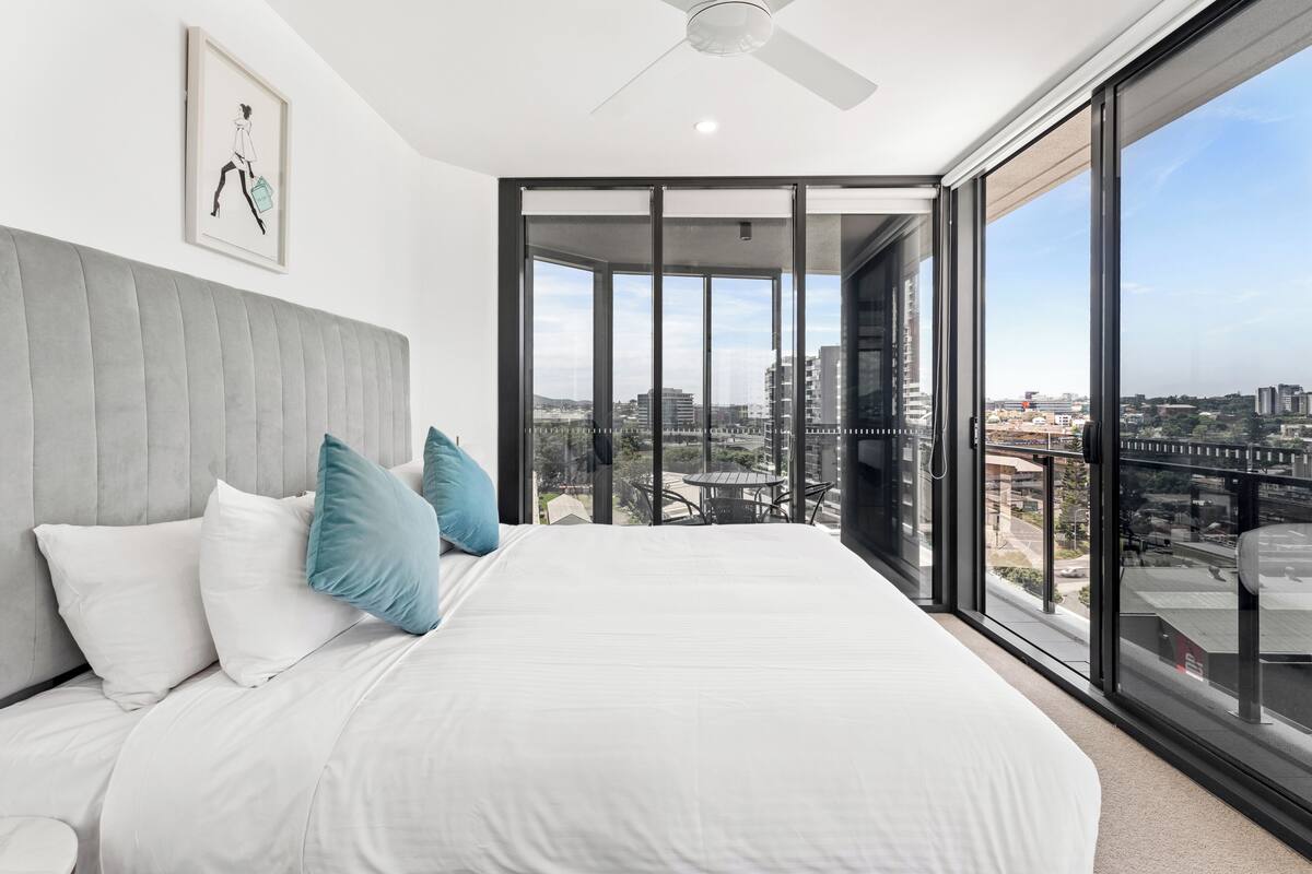Un dormitorio moderno con una cama grande, vistas a la ciudad y un balcón con mesa y sillas.