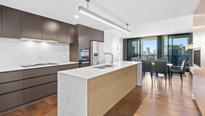 A modern kitchen with a marble countertop, dark cabinets, and a large island with a sink. - Brisbane One Apartments by CLLIX (South Brisbane)