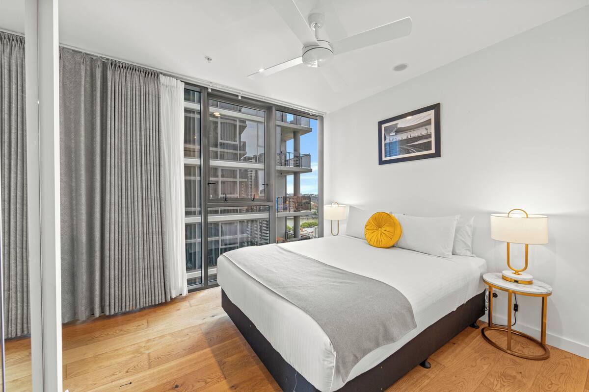 Un dormitorio moderno con una cama grande, ventilador de techo, ventana con cortinas y vistas al balcón.
