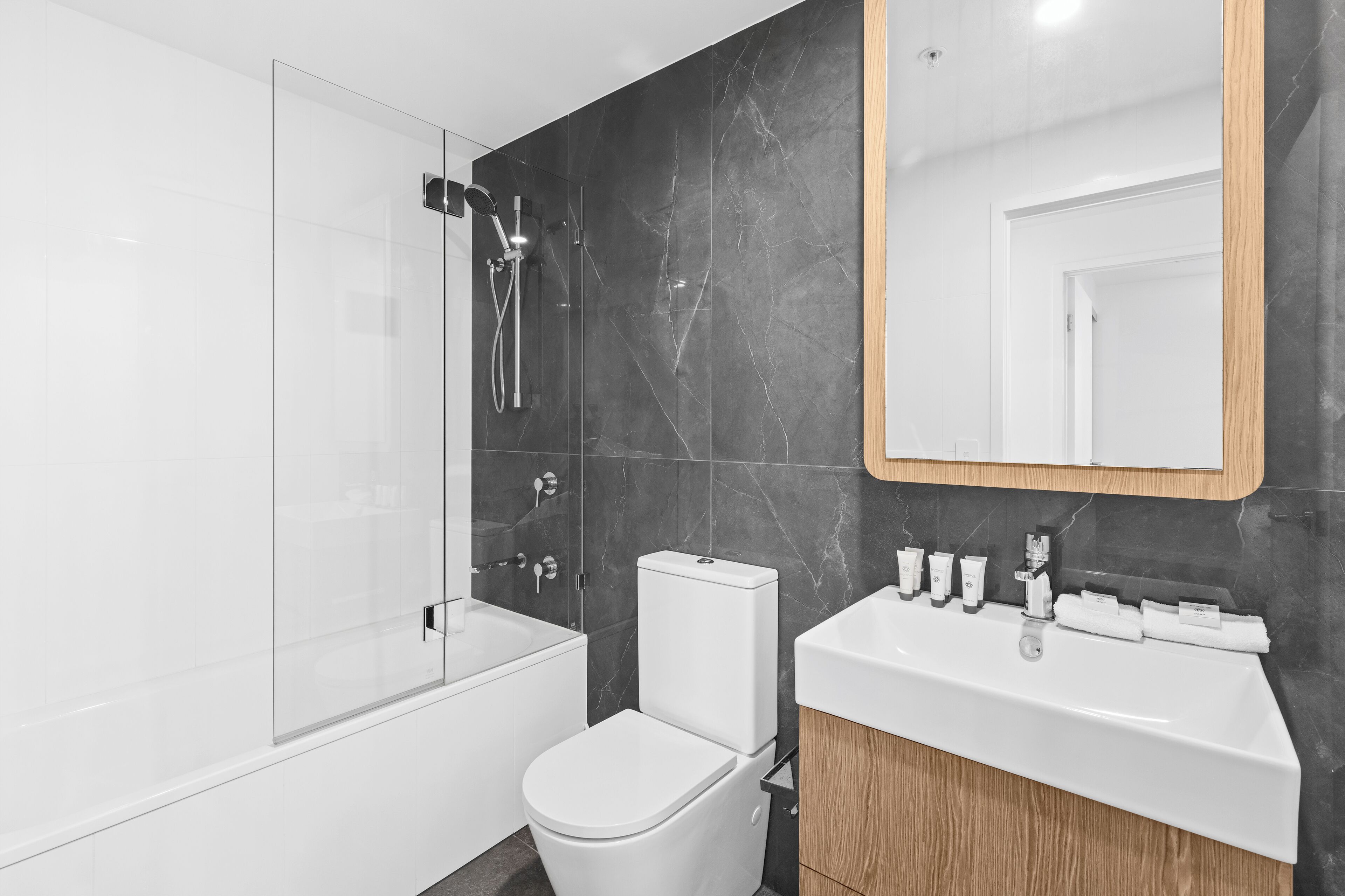Une salle de bain moderne avec une douche à parois de verre, des toilettes blanches, un meuble-lavabo avec un miroir et un lavabo agrémenté d’articles de toilette.