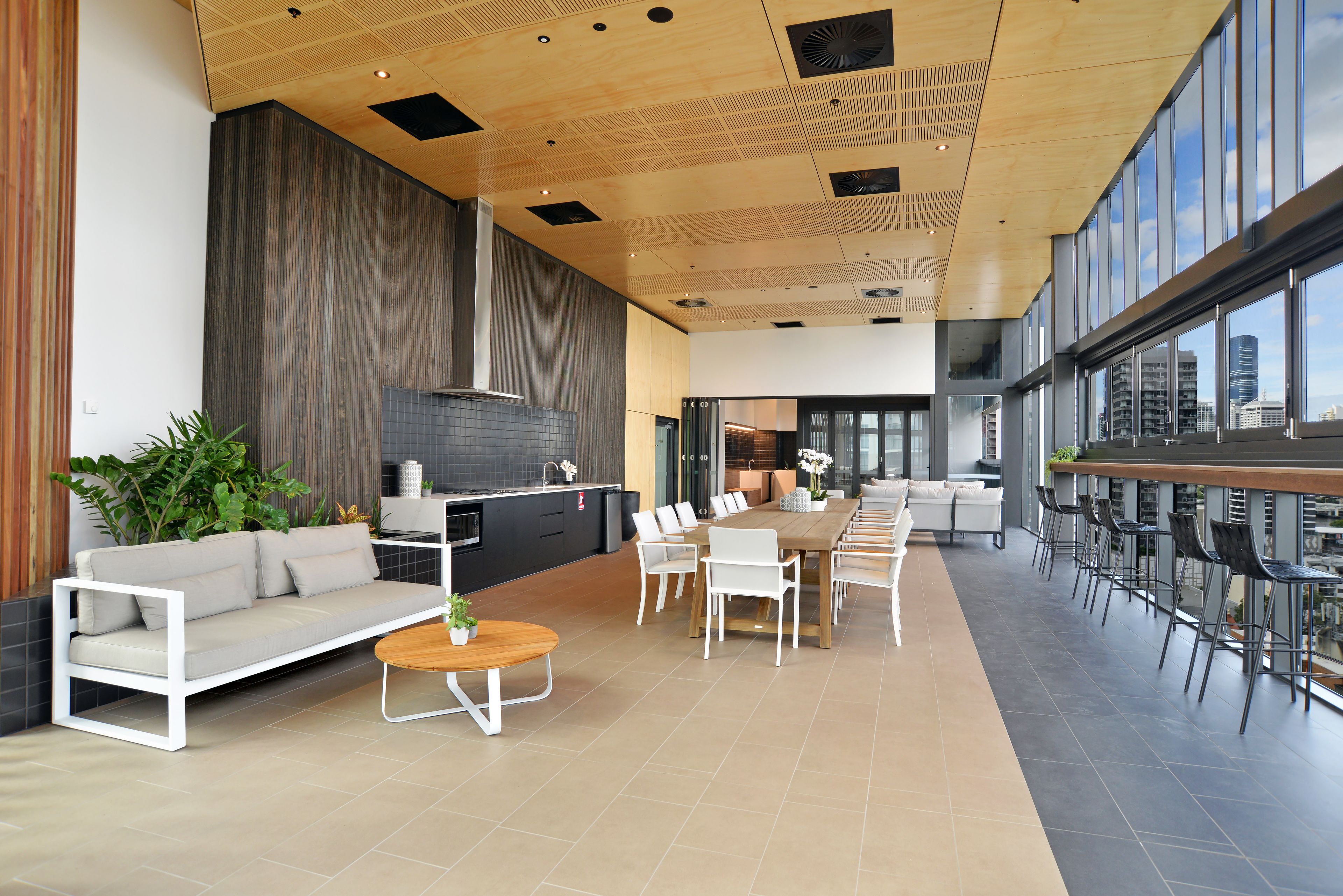 Un espacio interior amplio con una larga mesa de comedor, sofás blancos y una zona de bar con taburetes altos.