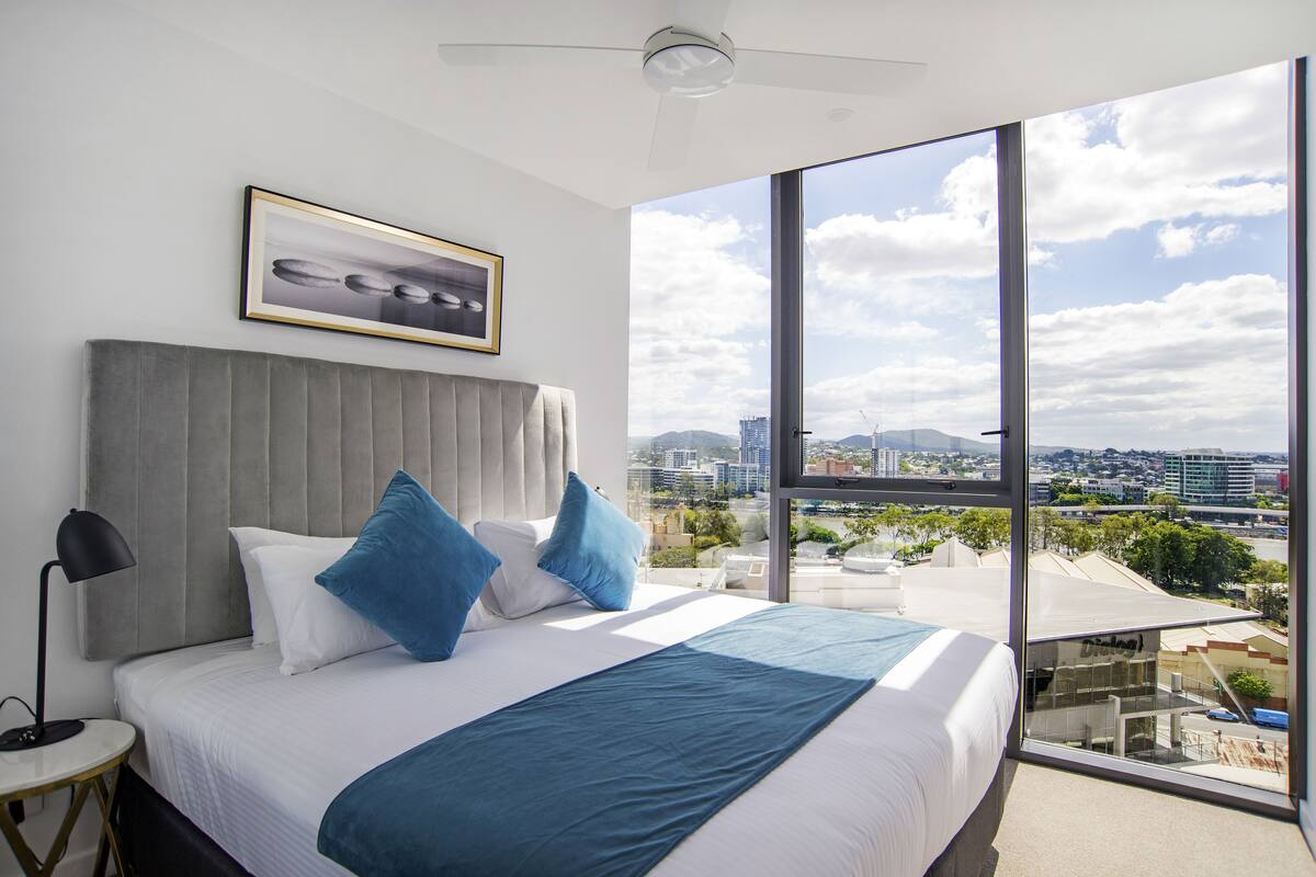 Una habitación de hotel moderna con una cama grande, vistas a la ciudad y un cuadro enmarcado en la pared.
