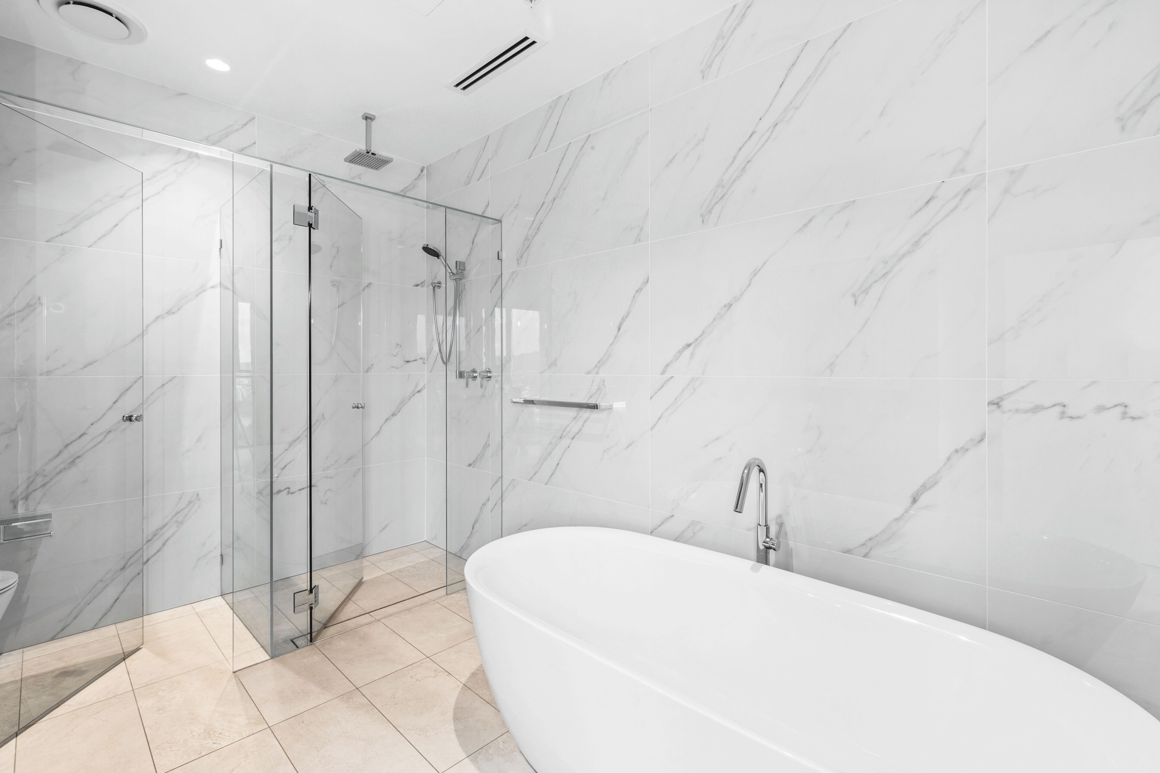 A modern bathroom with a glass-enclosed shower, a freestanding bathtub, and marble walls.