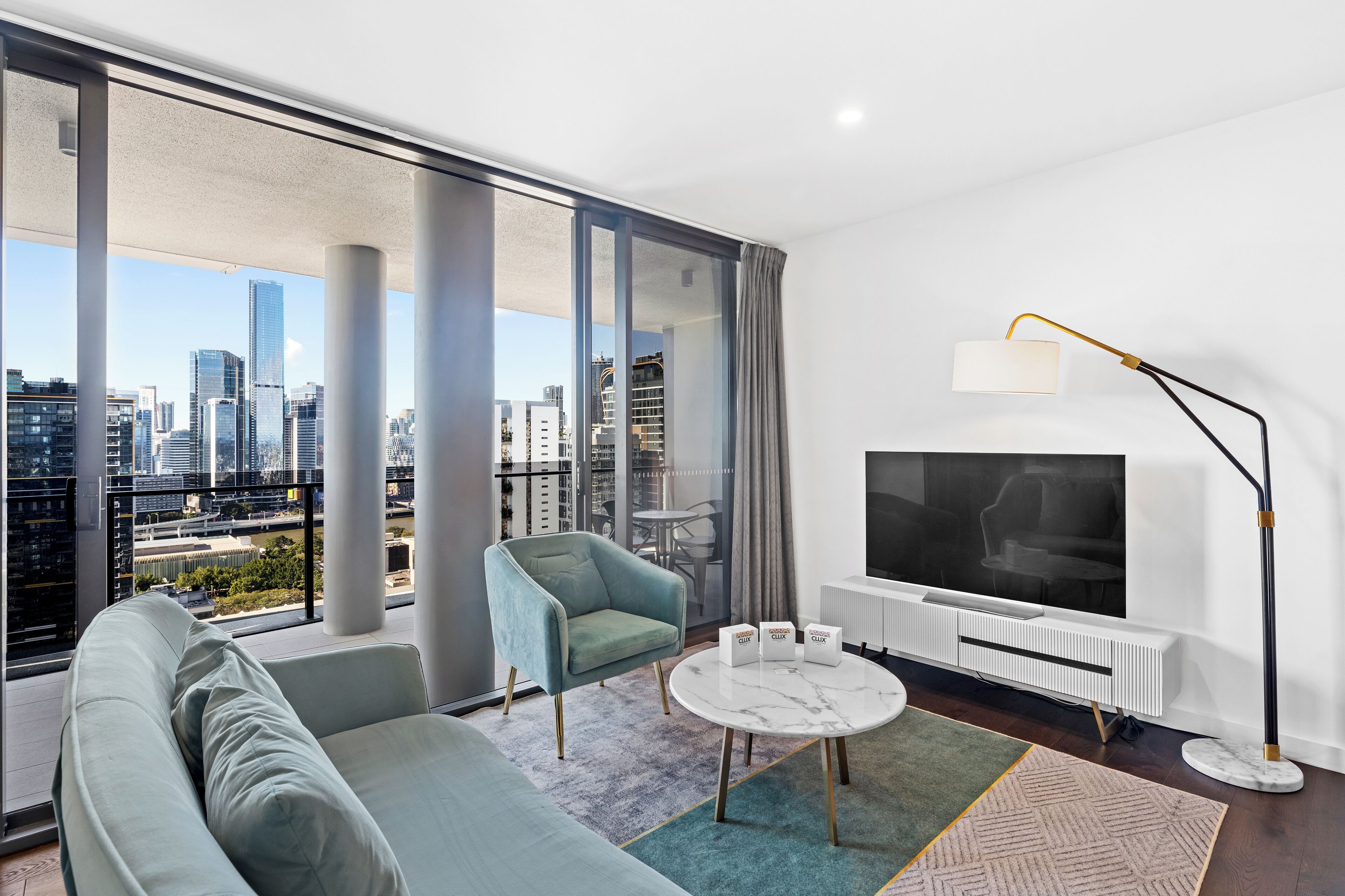 A modern living room with a large window, a sofa, a chair, a small table, and a TV.