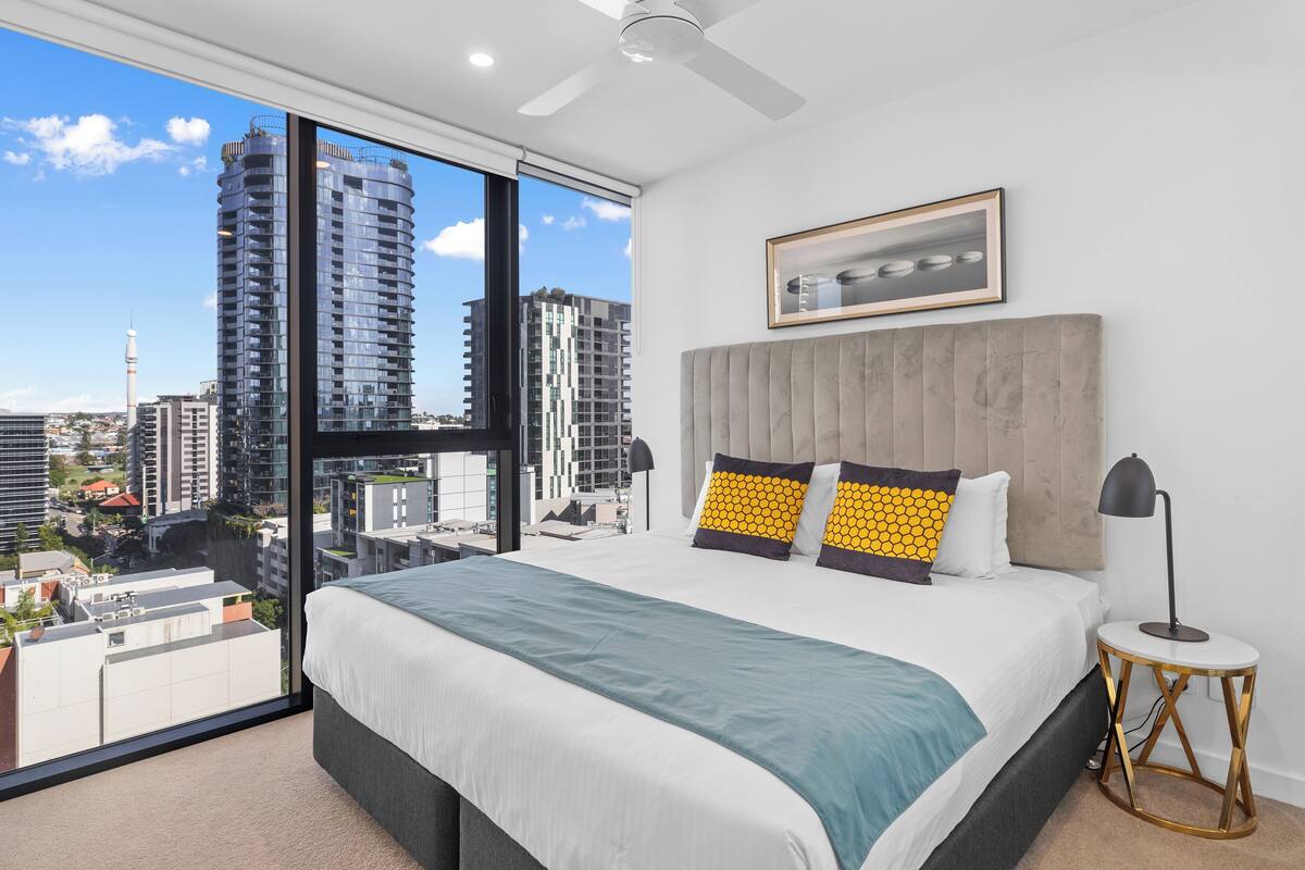 Una habitación de hotel moderna con una cama grande, vistas de la ciudad y un ventilador de techo.