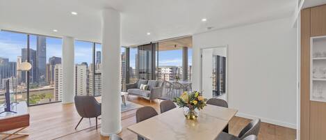 A modern living room with a large window, a dining area with a marble table, and a city view.