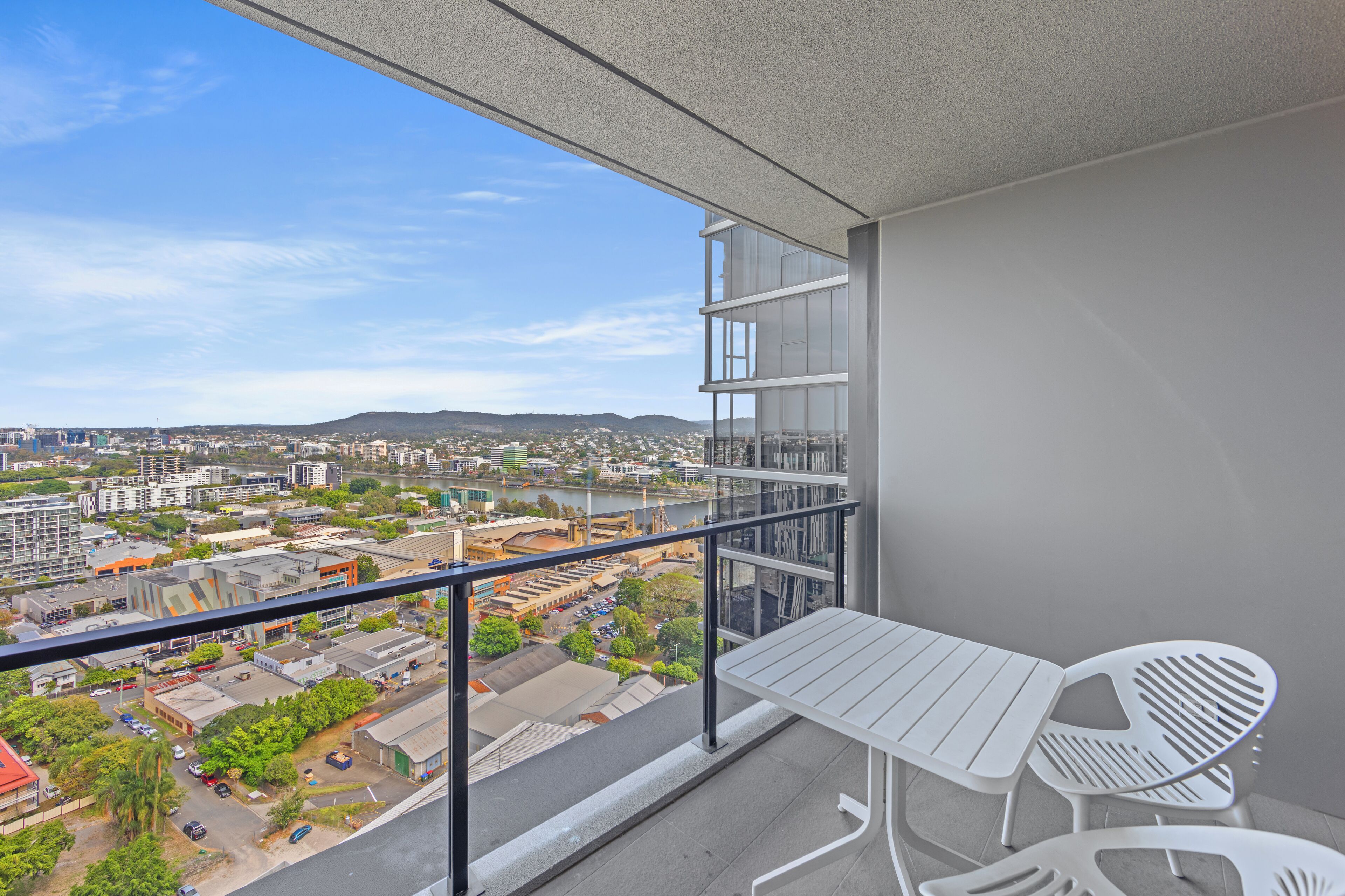 A balcony with a table and chairs, overlooking a cityscape with buildings and a river.