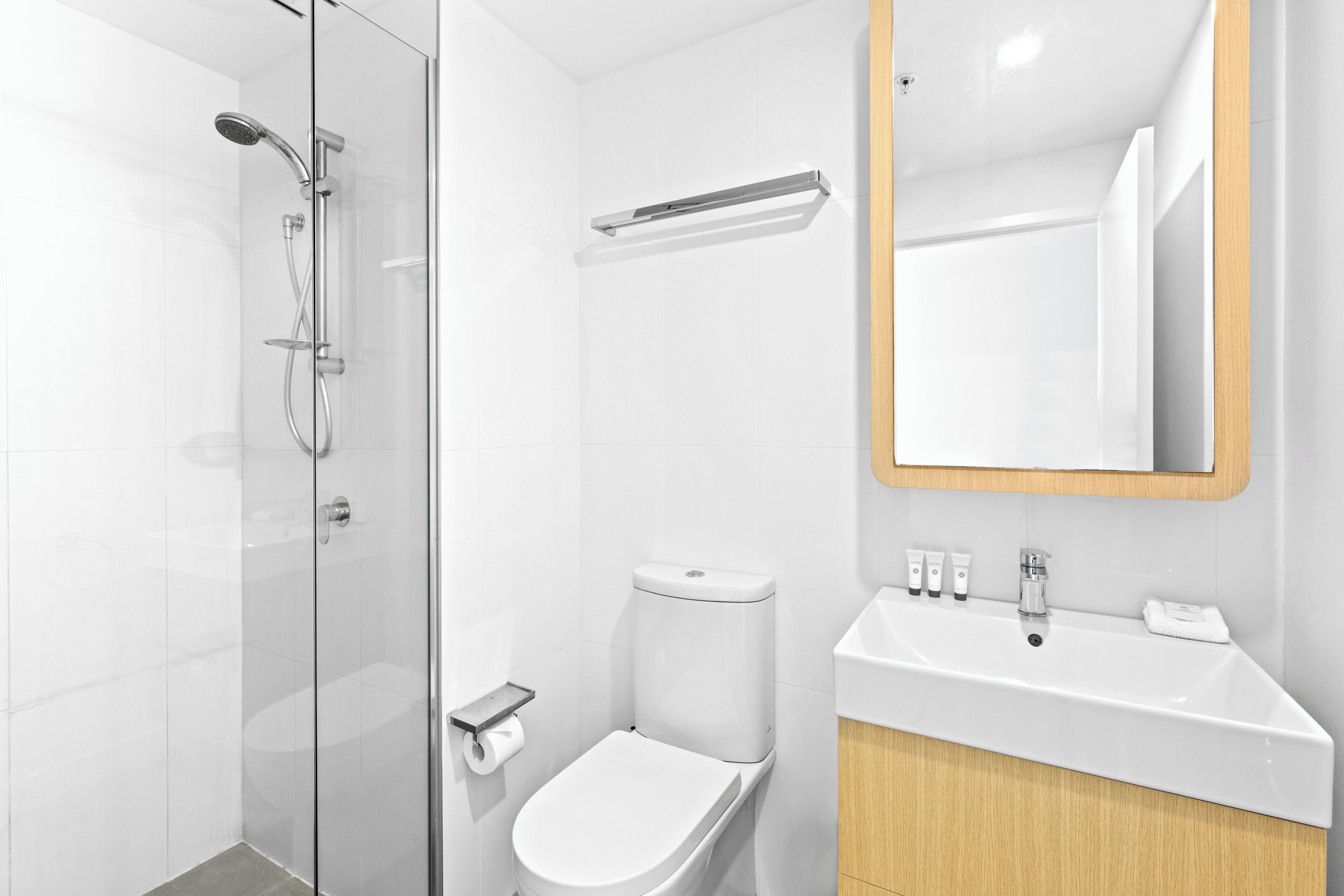 A modern bathroom with a glass-enclosed shower, a toilet, and a sink with a mirror above it.