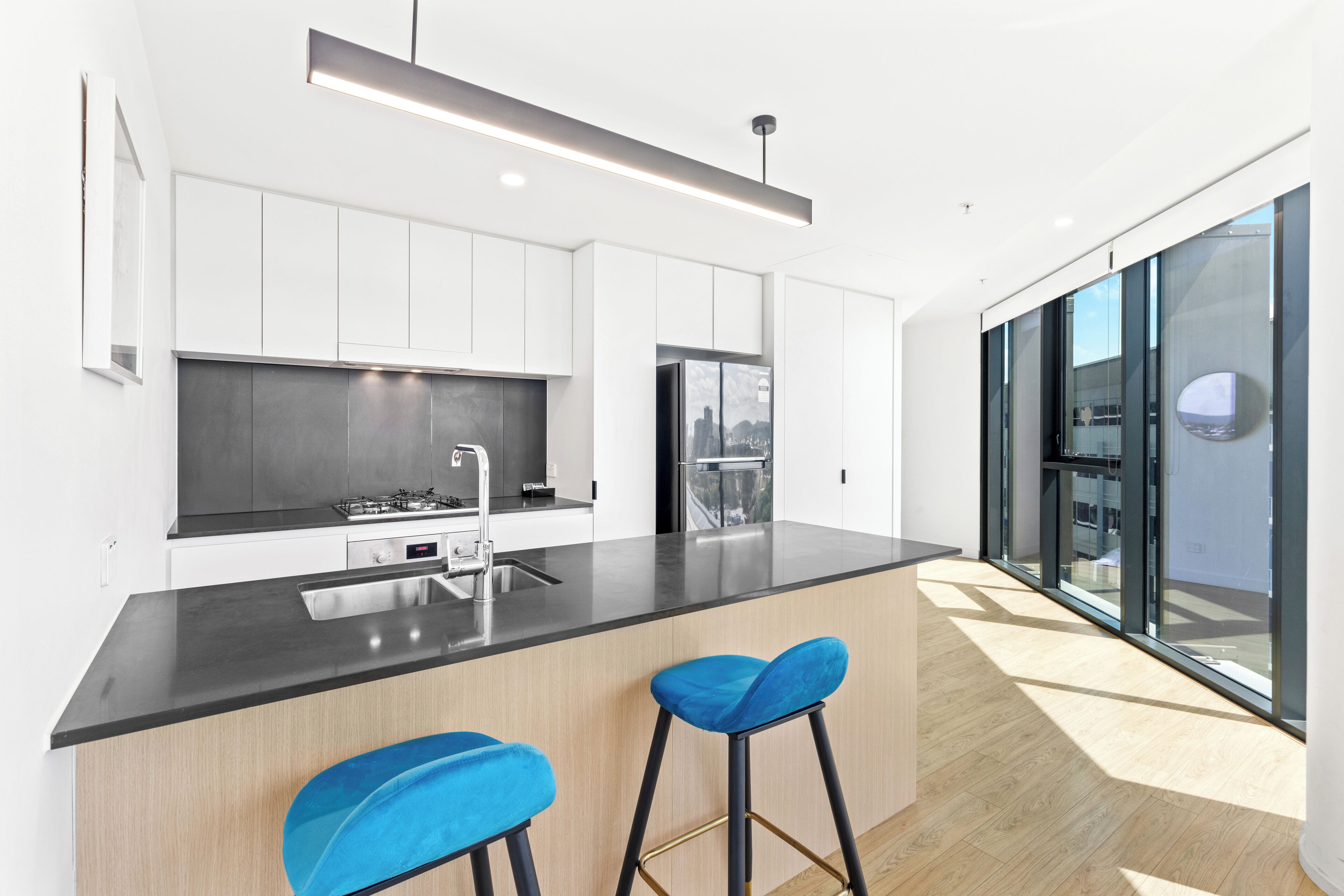 A modern kitchen with white cabinets, a black countertop, and two blue bar stools.