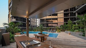 An outdoor pool area with a modern pool table, seating, and a view of a high-rise building. - Brisbane One Apartments by CLLIX (South Brisbane)
