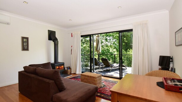 Una sala de estar acogedora con un sofá, una mesa de madera y una chimenea. Hay un balcón con sillas y un televisor.