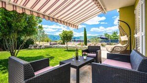 An outdoor patio with wicker furniture, a table with a bottle and glasses, and a view of mountains and greenery. - Lovely home in Donji Prolozac with sauna (Donji Prolozac)