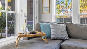 Un salon avec un canapé gris, un plateau en bois sur lequel se trouvent un verre de vin, des raisins et un citron, et un tableau encadré accroché au mur.