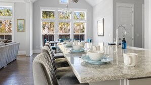 Une cuisine spacieuse dotée d’un grand îlot central, de grandes fenêtres et d’un coin repas avec des chaises en cuir.
