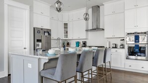 Une cuisine moderne avec des meubles blancs, des appareils en acier inoxydable et un îlot central doté de tabourets de bar.