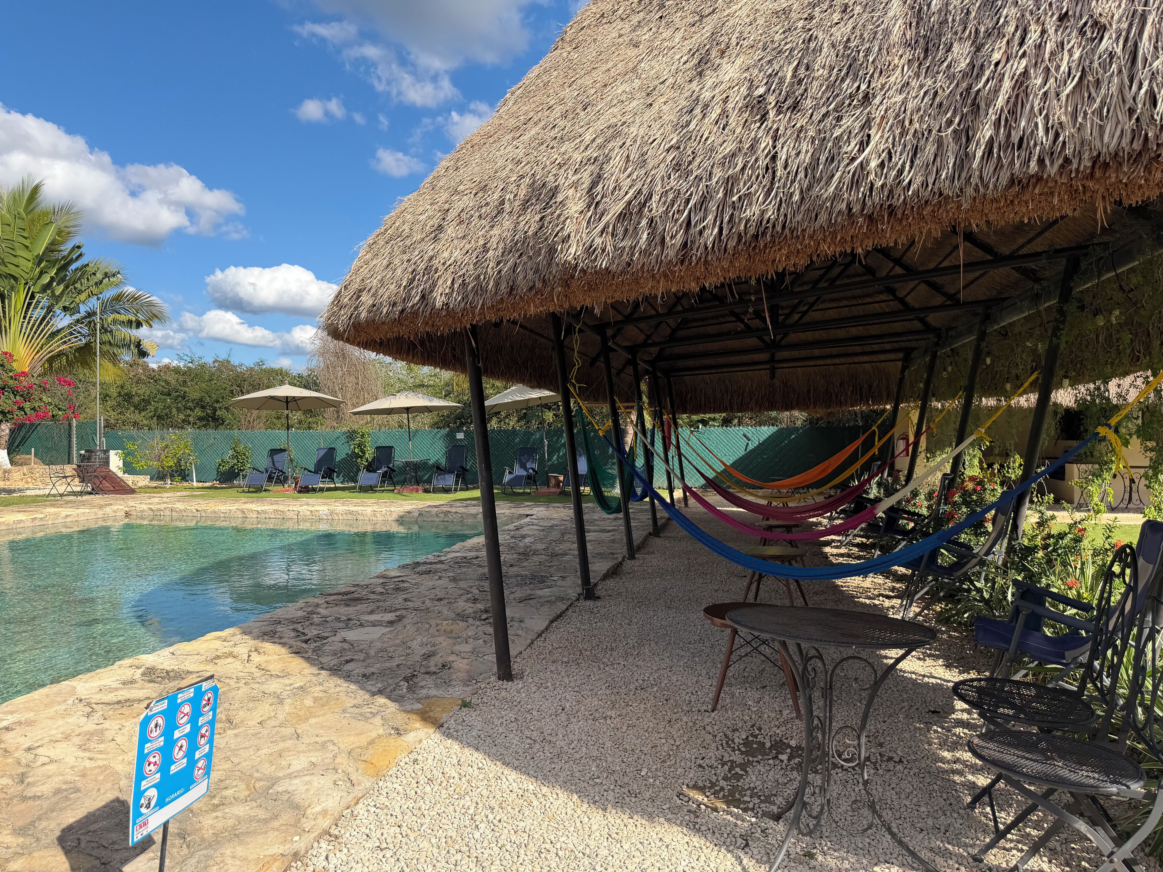 A pool area with a thatched roof structure, lounge chairs, and a hammock.