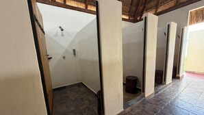 A bathroom with a tiled floor, a shower, and a trash bin.
