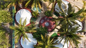 An aerial view of a resort with multiple white umbrellas, palm trees, and a central seating area with a red circular design.