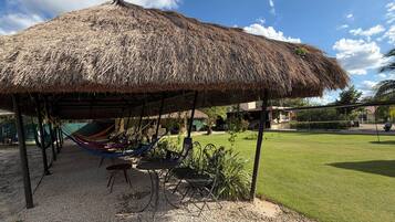 Un área de estar al aire libre con techo de paja, una hamaca y una mesa con sillas.