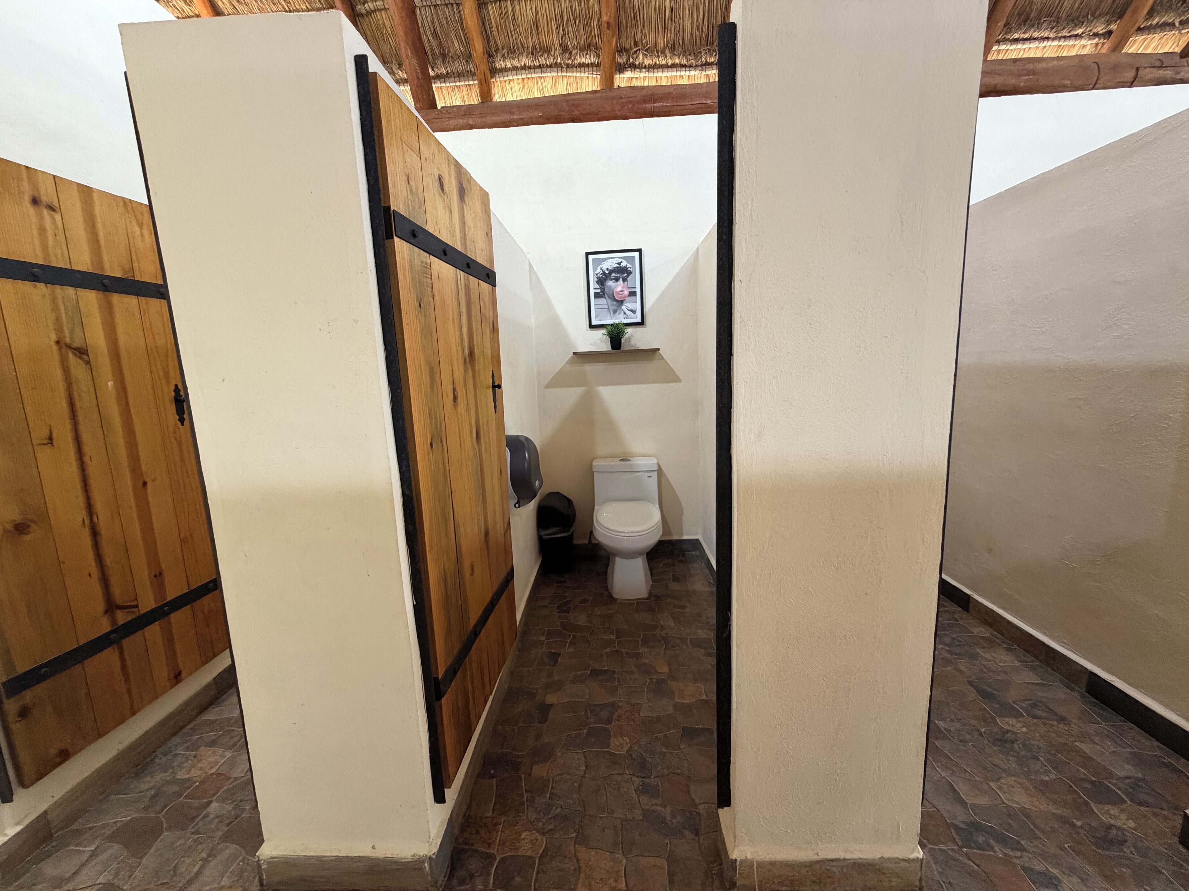 Eine Toilette mit Holztrennwänden, einer weißen Toilette und einem kleinen Regal mit einem gerahmten Bild.