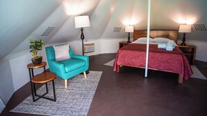A bedroom with a bed, two bedside tables, a chair, a small table, and a potted plant.