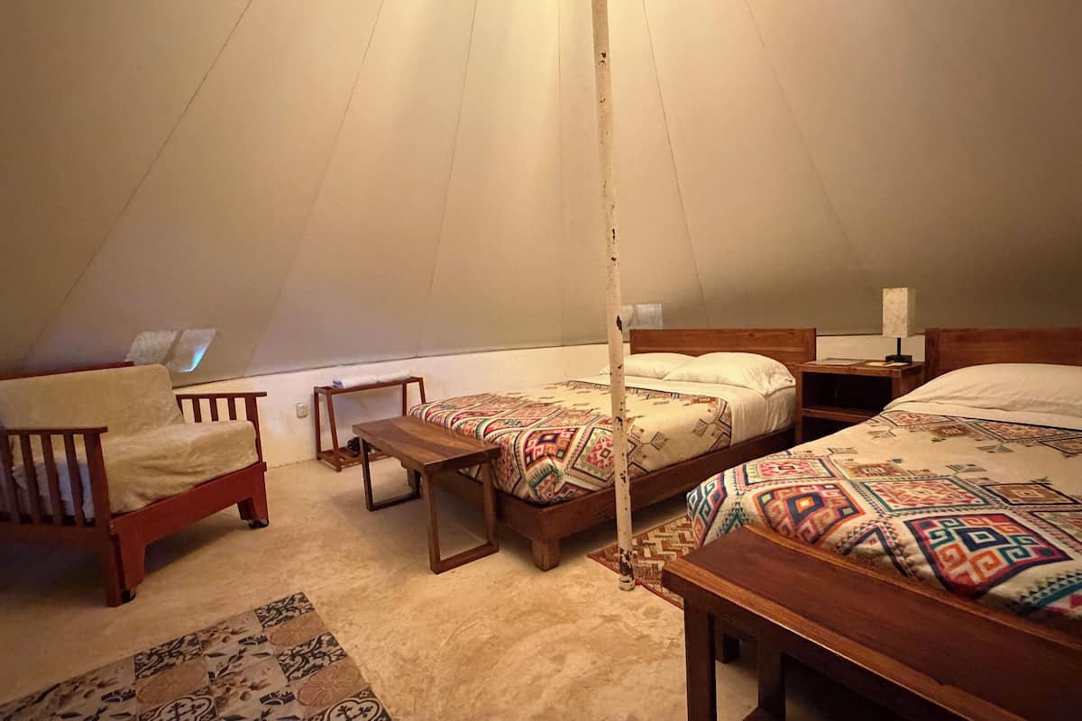 A cozy, well-lit tent with a single bed, a wooden chair, and a small table.