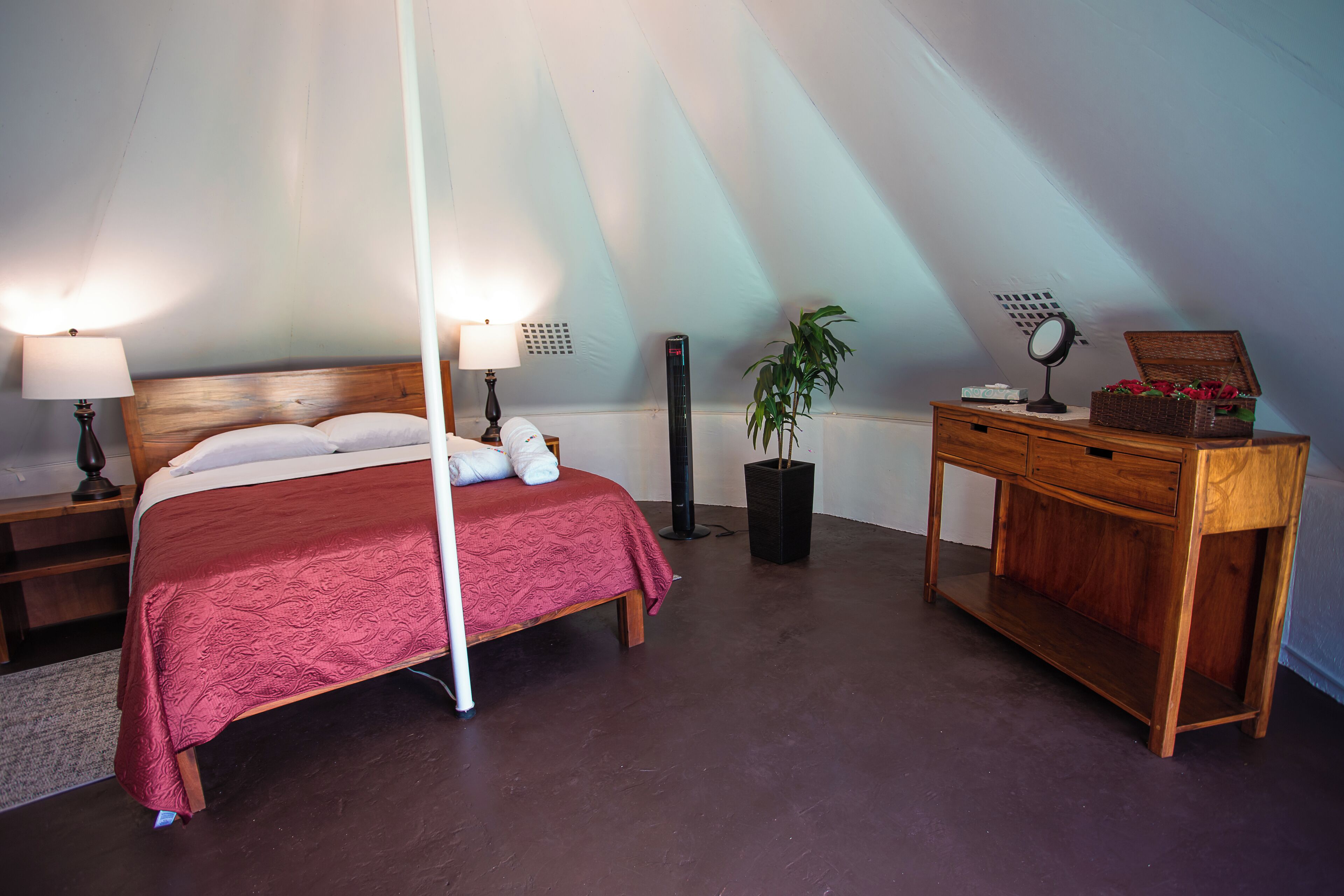 Une chambre à coucher avec un lit en bois, deux tables de chevet avec des lampes, une table de nuit, une commode, un miroir et une plante en pot.