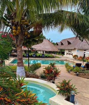 A pool area with a palm tree, thatched-roof structures, and lounge chairs.