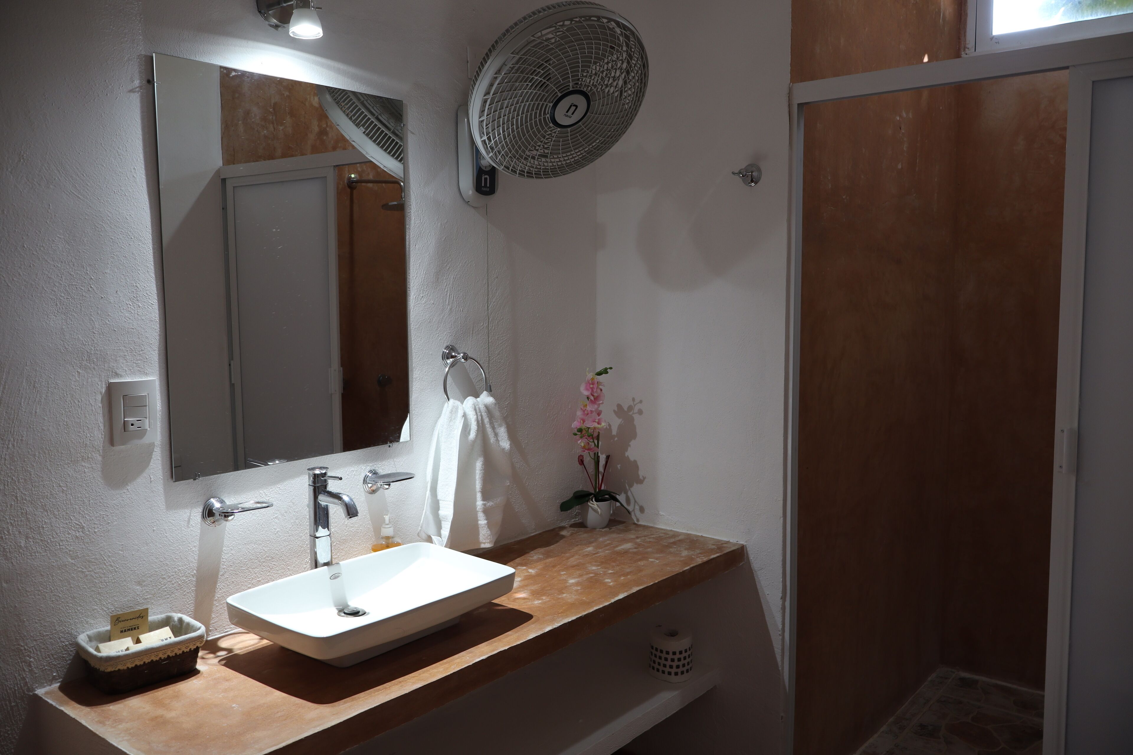 A bathroom with a white sink, a mirror, a towel rack, a fan, and a shower area.