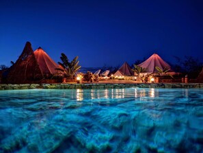 A nighttime resort with a swimming pool, thatched-roof structures, and well-lit pathways. - Hameki- Glamping (Homún)