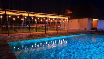 A swimming pool with a canopy and string lights at night.