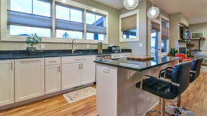 A modern kitchen with white cabinets, a central island with bar stools, and large windows with blinds. - Boutique-Style Retreat in Reynolds Village (Asheville)