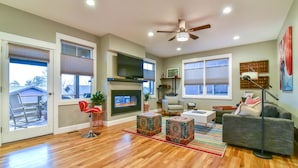 A spacious living room with hardwood flooring, a fireplace, a ceiling fan, and a large window. - Boutique-Style Retreat in Reynolds Village (Asheville)
