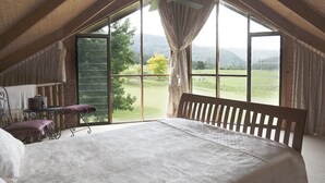 A bedroom with a large window, a wooden bed, a small table with a chair, and a view of a green landscape. - Cloud Nine Chalet - Luxury retreat in Upper River! (UPPER KANGAROO RIVER)