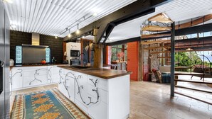 A modern kitchen with a central island, built-in appliances, and a large window overlooking a garden. - Lyra - Kangaroo Valley (KANGAROO VALLEY)