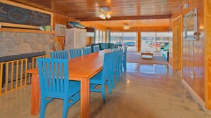 A cozy cabin interior with a wooden dining table and blue chairs, a stone wall, and a view of the outdoors. - Lakefront • Hot Tub • Walk to Beach & Downtown (Lake Odessa)