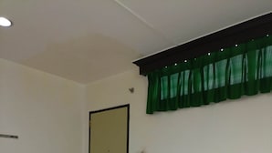Une chambre d’hôtel avec deux lits, un rideau vert, une porte avec un avis affiché et un mur blanc.