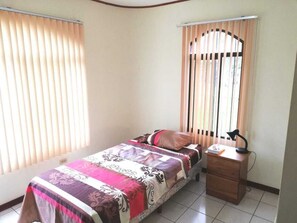 A bedroom with a bed, a nightstand, a lamp, and a window with blinds.
