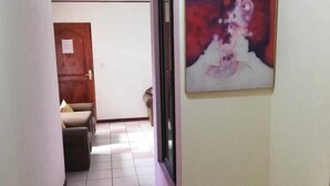 A hallway with a tiled floor, a framed painting on the wall, and a door at the end.